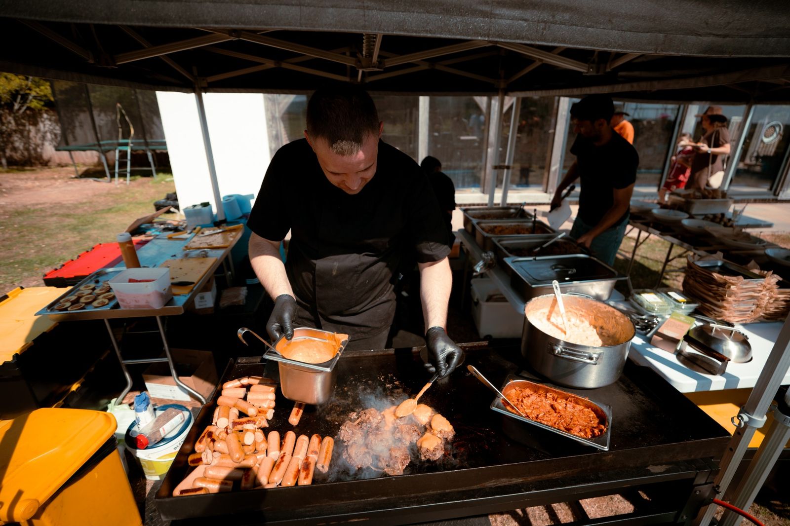 Chef cooking burgers and hot dogs on the griddle at a garden party